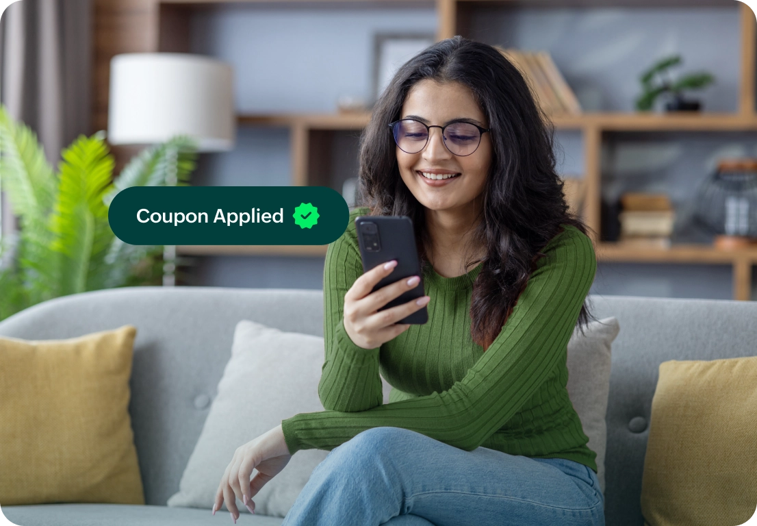 A woman happily checks her phone with a digital banner that reads Coupon Applied.